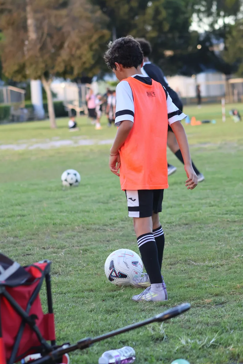 A player in an orange bib waits beside a training ball