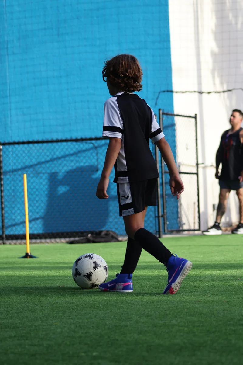 A player in black controls a ball beside the blue building