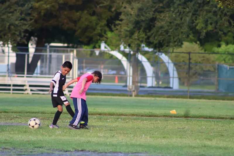 Two players, one in a pink bib, challenge for possession