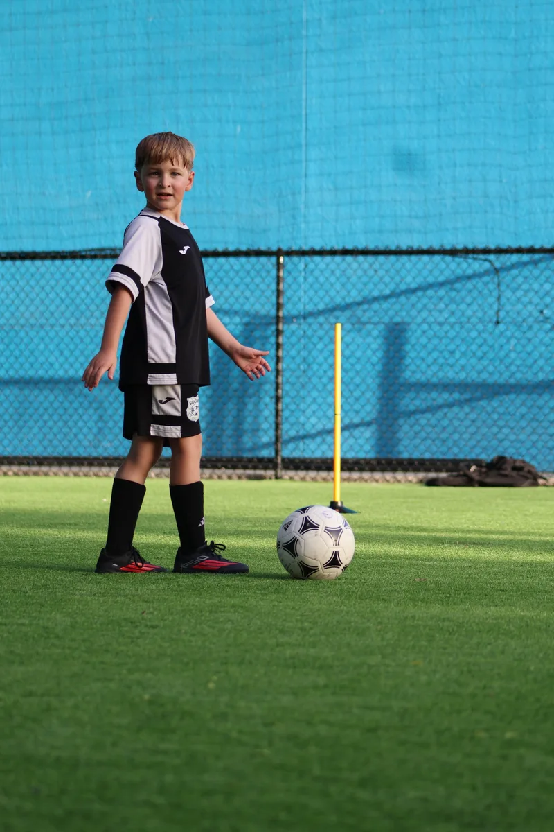 A young player stands beside a ball on the green turf