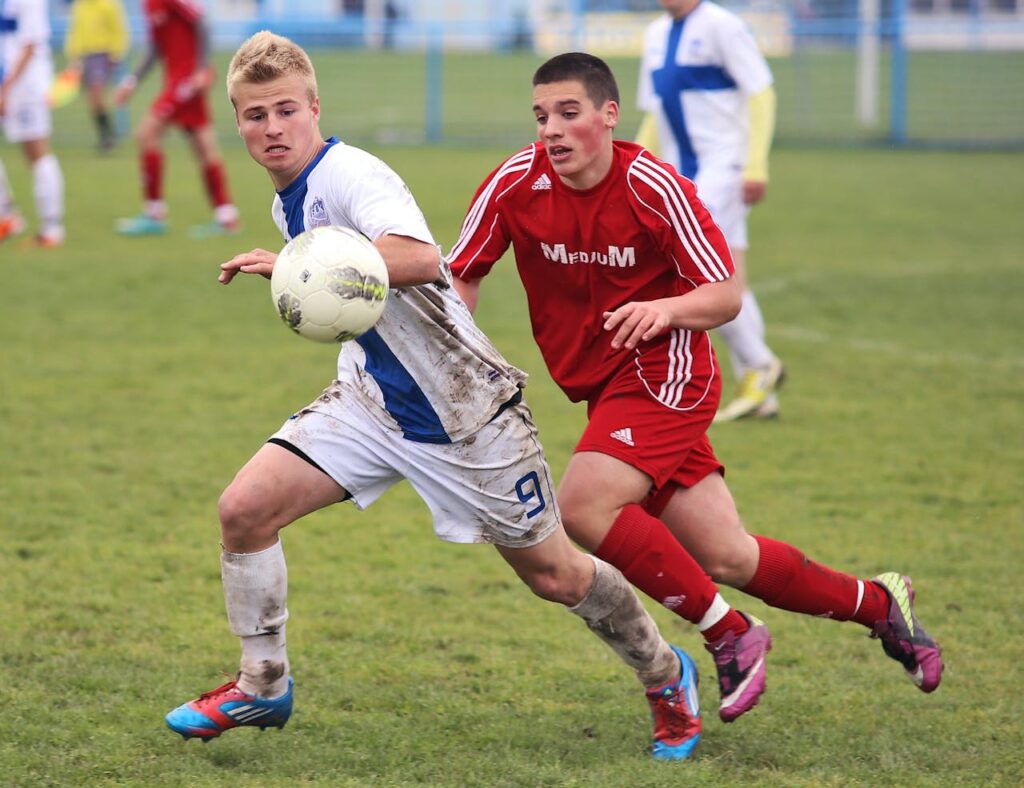 people-men-grass-sport Two teenage soccer players competing fiercely on a muddy grass field.