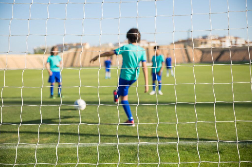 pexels-photo-8941639 Group of children playing soccer on a sunny day in Portugal, seen through the goal net.